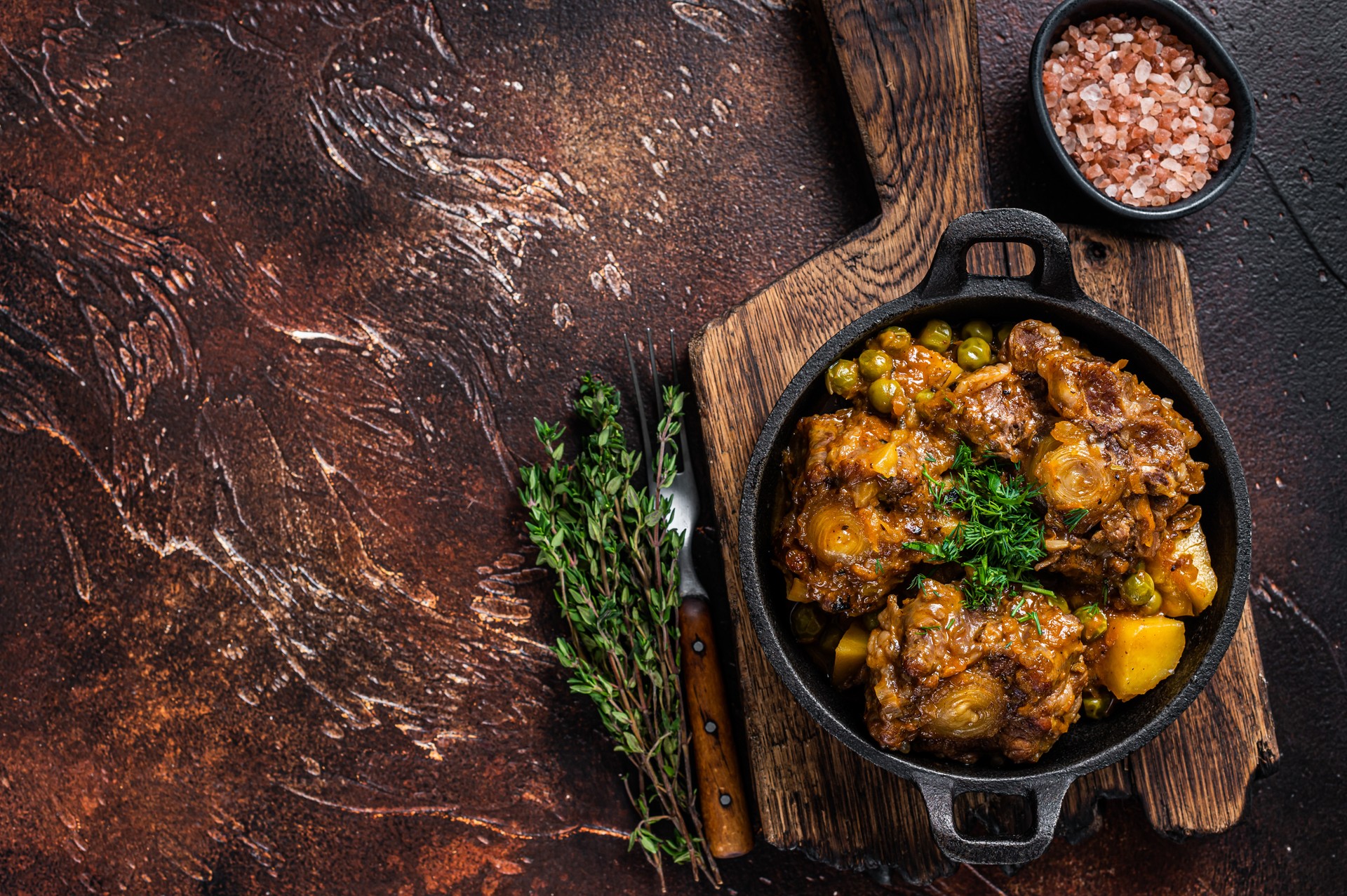 Beef oxtails stew with wine and vegetables in a pan. Dark background. Top view. Copy space